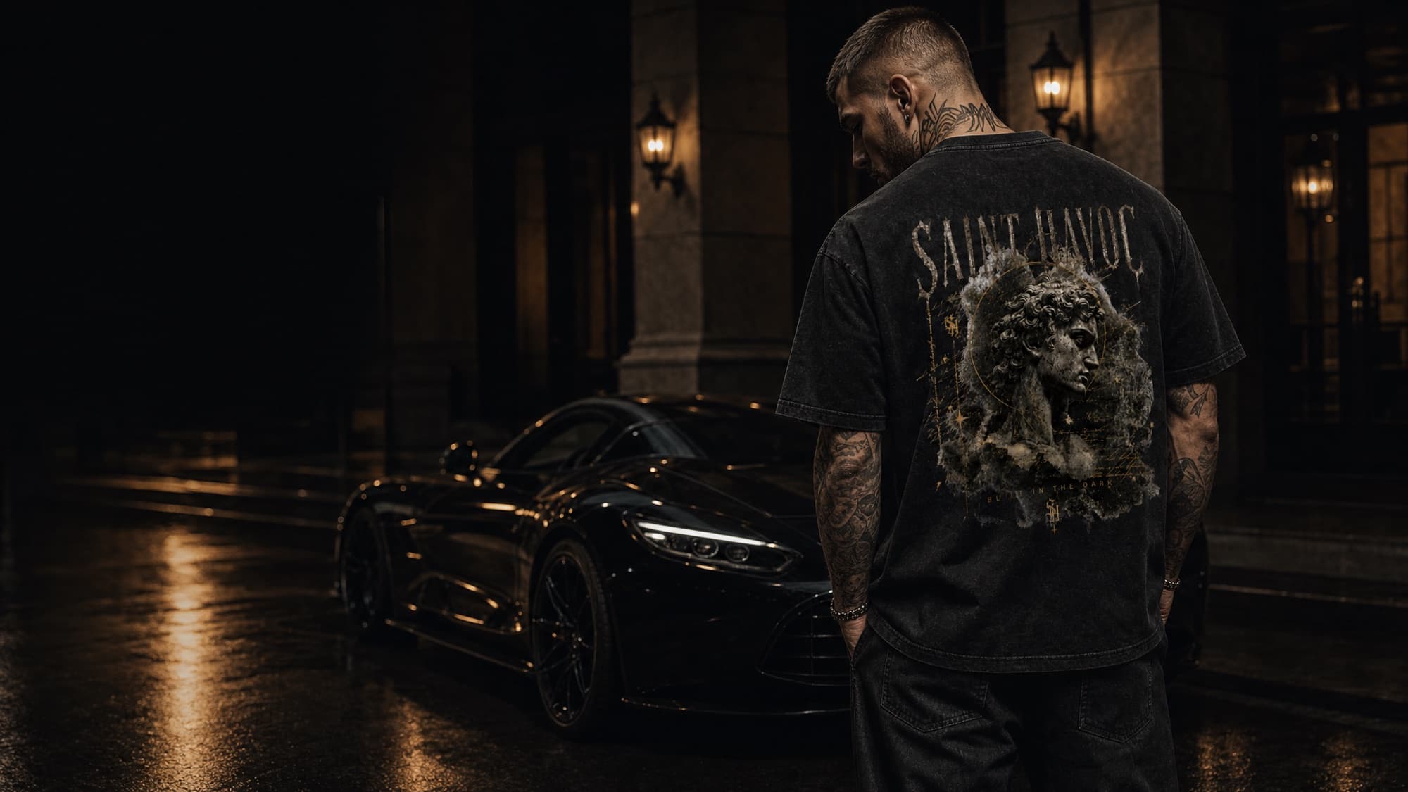 A man wearing a washed black Saint Havoc graphic tee at night